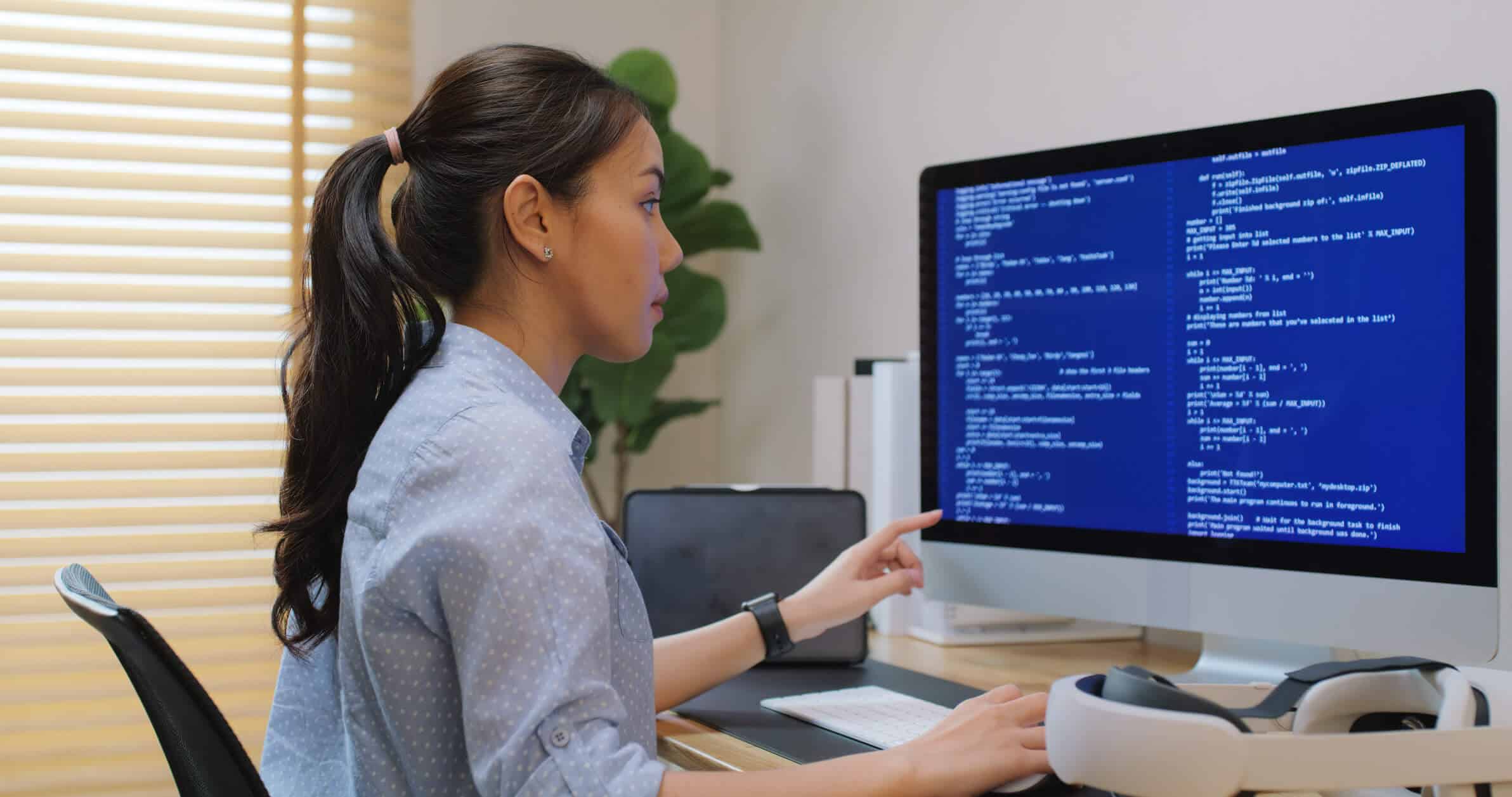 A woman reviewing code on a desktop computer while studying cybersecurity concepts