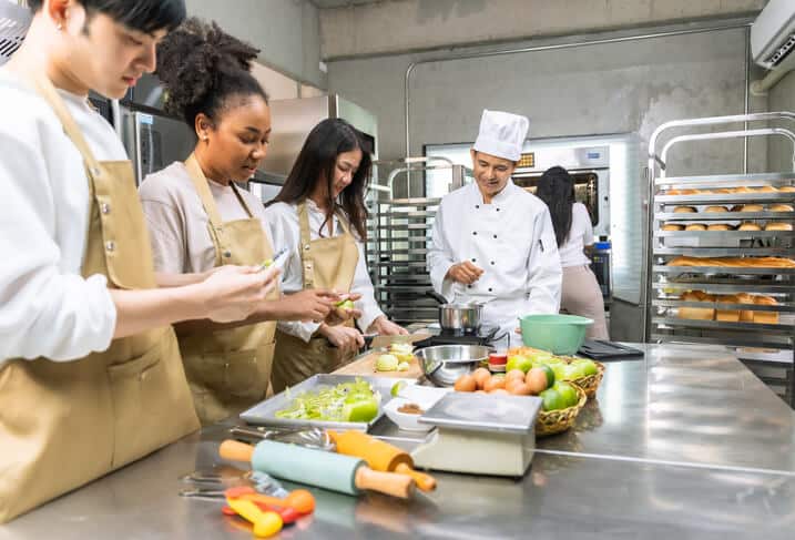 A group of students in a food and nutrition training program practicing meal prep techniques in a classroom kitchen