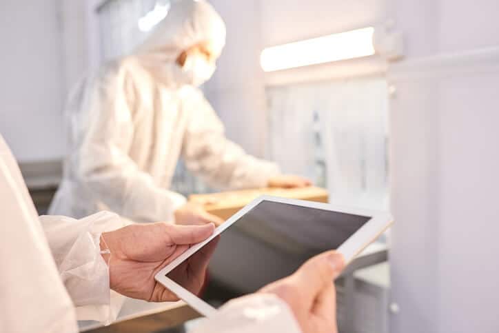 Laboratory researchers in protective clothing documenting their work on a tablet
