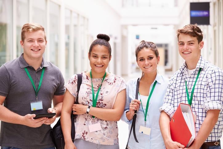 Four students wearing lanyards standing together in a college hallway