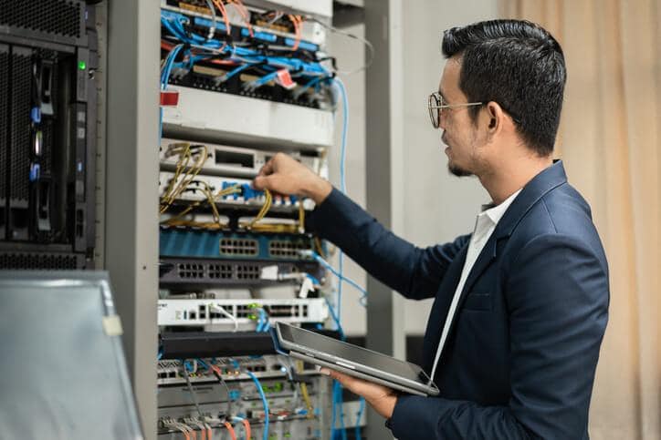 An IT support professional is configuring a network switch in the server room, showing the network fundamentals for information technology