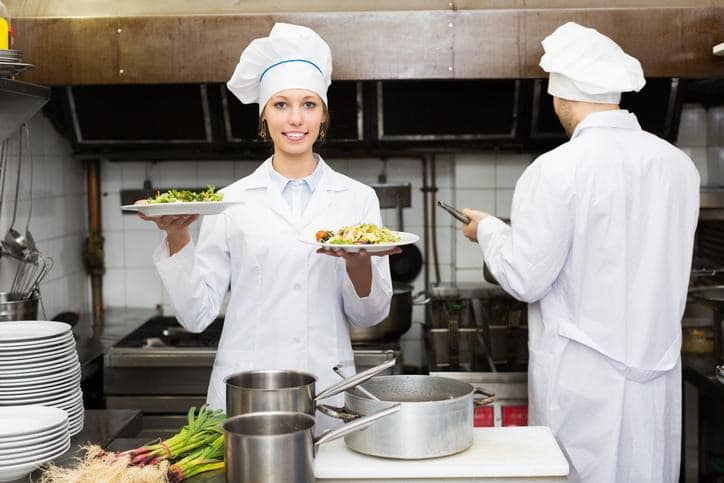 Two food service professionals preparing and plating meals in a commercial kitchen