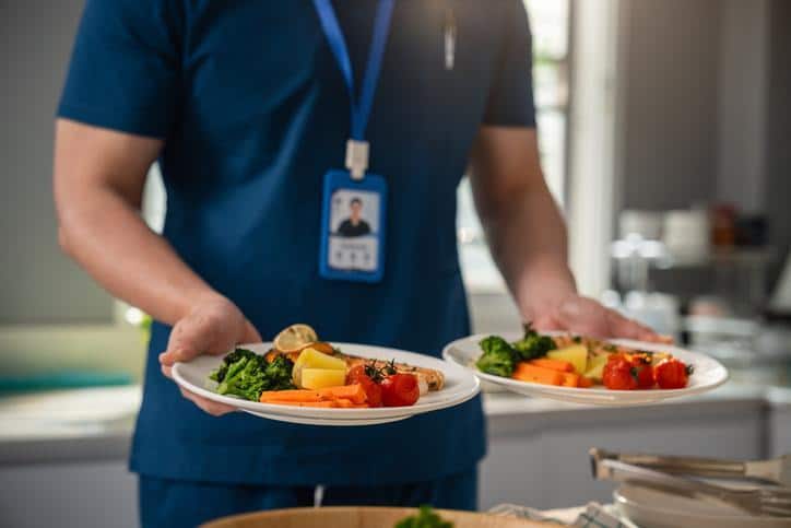 A healthcare worker carrying two plated meals with vegetables